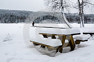 Two people looking at the landscape. Wood bench and table covered of snow in front of a frozen lake photo