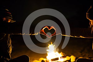 two people making heartshape with hands over a campfire at night