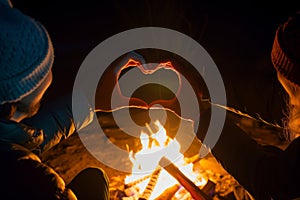 two people making heartshape with hands over a campfire at night