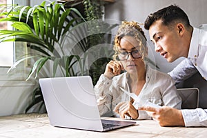 Two people male female working together in home office workplace with laptop and documents. Young man and adult woman team using