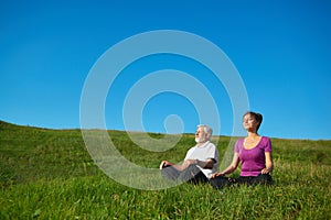 Two people meditating sitting in the field.