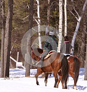 Two people out horseback riding in the cold snow