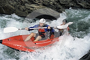 Two people paddling inflatable boat down rapids