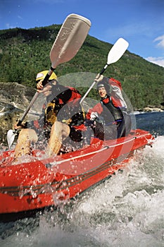 Two people paddling inflatable boat down rapids