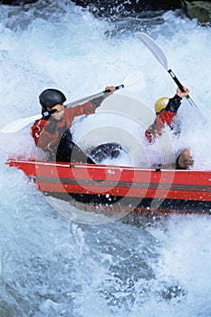 Two people paddling inflatable boat down rapids