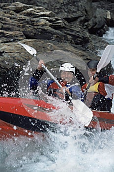 Two people paddling inflatable boat down rapids