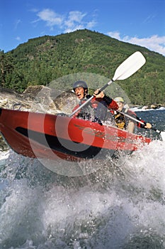 Two people paddling inflatable boat down rapids