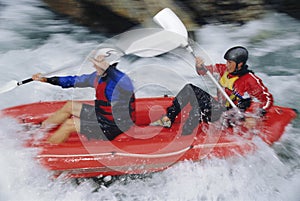 Two people paddling inflatable boat down rapids