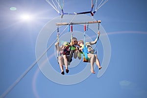 two people parasailing on beach in summer. Happy couple kissing under parachute in air above surface of the sea