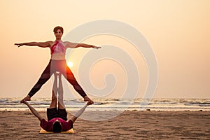 Two people practicing yoga in the sunset light on goa india beach. female and male acro yogi tantra flying copyspce