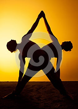 Two people practicing yoga in the sunset light