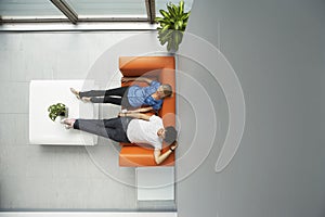 Two People Reclining On Orange Sofa At Office