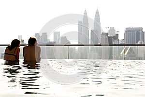 Two people reclining in a pool in a building overlooking the city of Kuala Lumpur