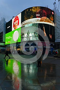 Two people with reflections in the wet pavement in Piccadilly at dusk