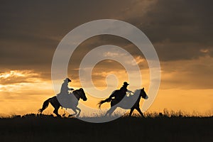 Two people riding horses on a grassy field at sunset in Bangkok, Thailand