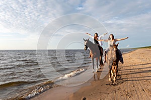 two people riding on swallowing the beach on horses at sunset