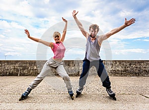 Two people on rollerblades with spread arms.