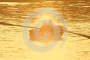 Two people in a rowboat flared by the golden evening sun.