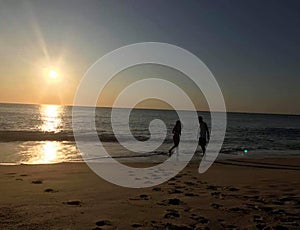 Two people running on the beach while the waves crash against the sand