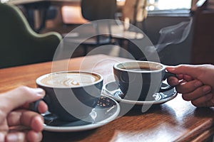 Two people`s hands holding coffee and hot chocolate cups on wooden table in cafe