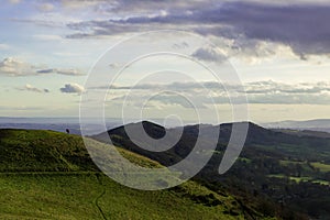 Two people silhouetted in the distance looking from the top of a hill on a sunny winters days. Malvern Hills, England