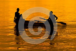 Two people in a small boat at orange and golden sunset