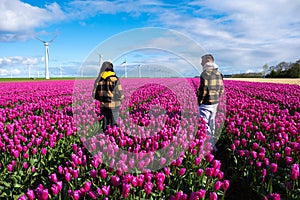 Two people stand amidst a vibrant field of purple tulips in the Dutch countryside, surrounded by towering windmill