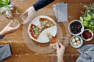 Two people toasting with wine one person eating pizza