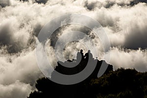 Two people on top of a mountain above the clouds