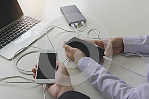 Two people using two mobile phone sharing USB Power Bank on a table to charge the mobile devices.Technology device charge sharing