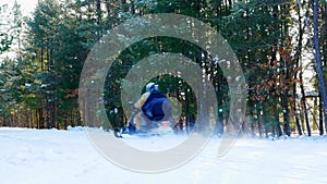Two people wearing helmets ride a snowmobile on a groomed trail past trees in a forest in Minnesota on a sunny winter day