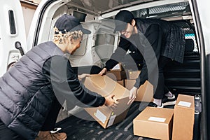 Two people working for delivery company unloading cardboard boxes from van