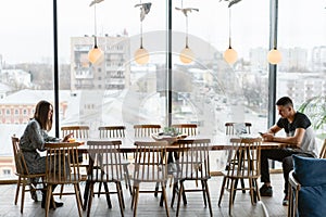 Two people a young man and a woman sitting at a big table, from different sides. distance between people. The concept