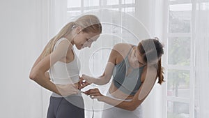 Two people young woman measuring waist for weightloss together at living room.