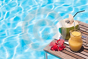 two perfect cocktails - fresh coconut and mango smoothie over pool background