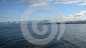 Two personal watercrafts racing on blue fjord with snowy mountain background.