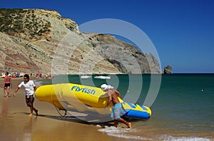 Two persons dragging at the beach an inflatable flyfish water attraction