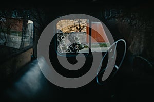 Two persons in NBC protective suits and gas masks, view through cabin of old truck