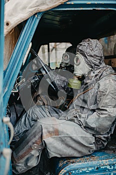 Two persons sits in NBC protective suits and gas masks in old truck