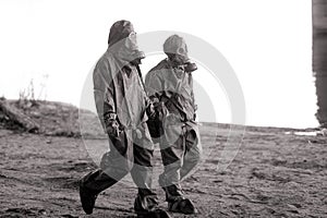 Two persons walks in NBC protective suits and gas masks