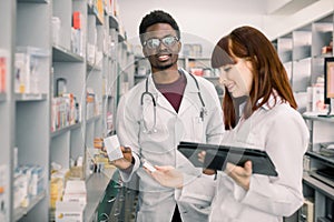 Two pharmacist looking for medicinal drug. Male African pharmacist holding a medicine with female standing by and using