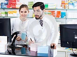 Two pharmacists are attentively stocktaking medicines with computer and note on paper