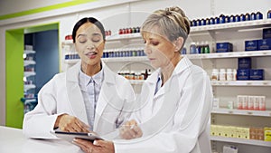 Two pharmacists scrolling on digital tablet locating medicines in pharmacy