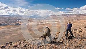 Two photographers in mountains. A gray-haired man in a camouflage jacket and a red-haired girl in a striped sweater photograph the