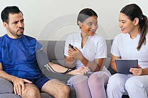 Two physicians checking a man`s blood pressure at home