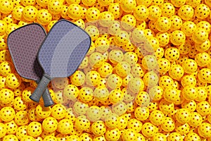 Two pickleball rackets lie on top of a large pile of yellow sports balls.