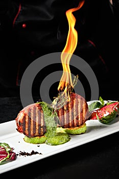 Two piece of meat in flame on the white plate