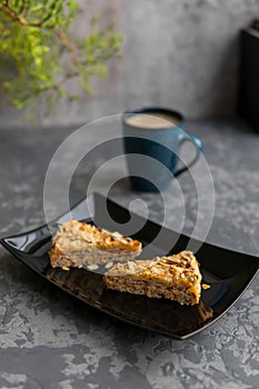 Two pieces of almond cake on black dish and mug of coffee. Selective focuse. Dark concrete background. Vertical photo