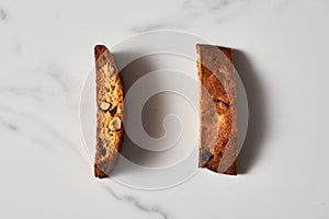 Two Pieces of Almond and Cranberry Biscotti Standing on Marble Counter, Shadowed with Natural Light
