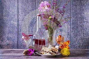 Two pieces of cake in plate, bottle of wine, wild flowers in vase and wine glasses stand on wooden table. Positive mood.